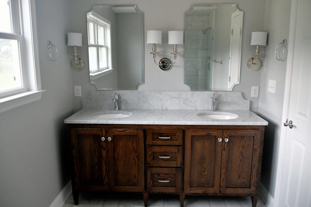 Clean bright bathroom with dark wood vanity and white marble sinks in a new home or after a remodel