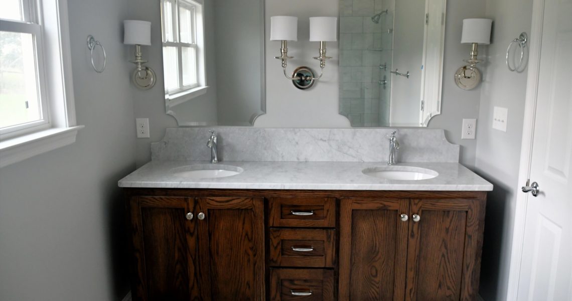 Clean bright bathroom with dark wood vanity and white marble sinks in a new home or after a remodel